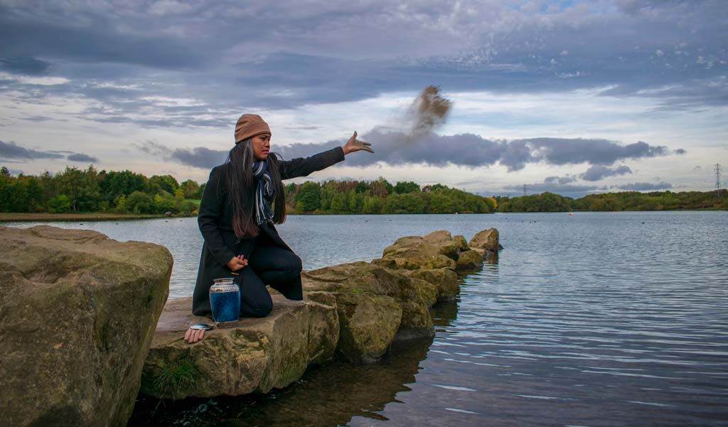 A person scattering ashes onto a lake from the rocks.